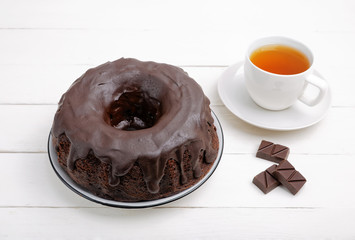 Homemade chocolate cake in the form of a ring and cup of tea on white wooden table. Angle view.