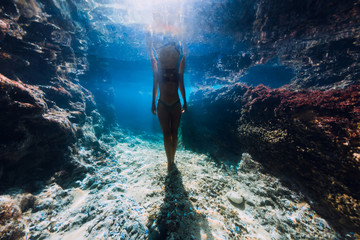 Woman in bikini posing underwater near corals in ocean.