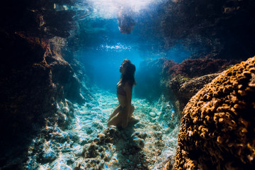 Woman in bikini posing underwater near corals in ocean.