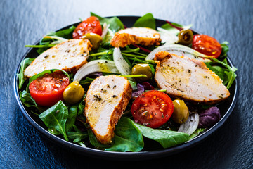 Caesar salad - barbecue chicken breast and vegetables on black stone board