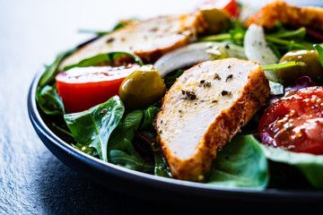 Caesar salad - barbecue chicken breast and vegetables on black stone board