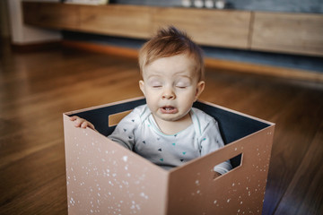 Adorable little caucasian blond boy sitting in box and sneezing. Home interior.