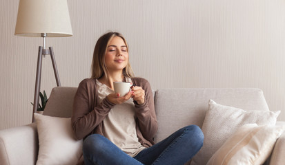 Positive young girl enjoying smell of fresh hot coffee
