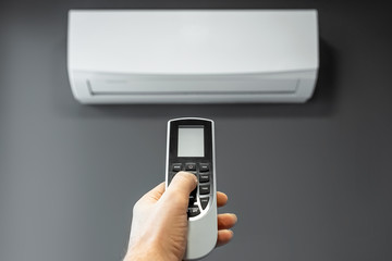 Hand with a remote control from an air conditioner close-up on a background of a white air...