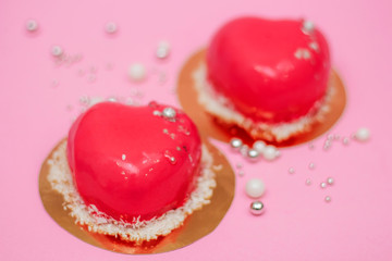 Two pink hearts, covered with mirror glaze and decorated with silver and white beads, lies on a pink background close-up. Holiday concept - Valentine's Day, Family Day, International Women's Day. 