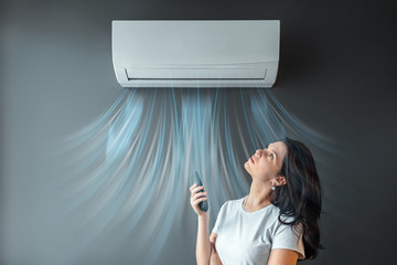 A beautiful girl stands under air conditioning and a stream of fresh cold air against a gray wall....