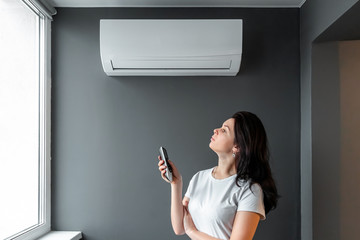 A beautiful girl stands under air conditioning and a stream of fresh cold air against a gray wall....