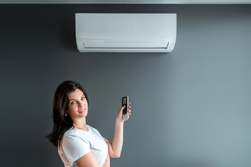 A beautiful girl stands under air conditioning and a stream of fresh cold air against a gray wall....