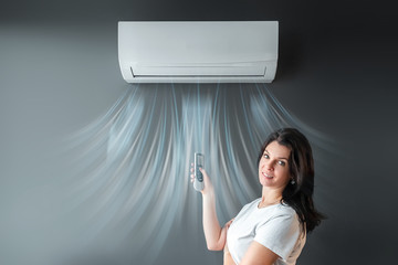 A beautiful girl stands under air conditioning and a stream of fresh cold air against a gray wall....