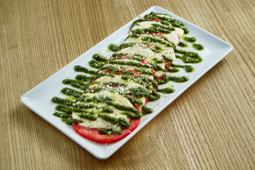 Close up view on Appetizing Italian caprese salad with fresh tomatoes, soft mozzarella, arugula and...