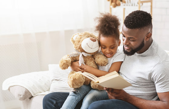Cute afro family father and daughter reading book at home