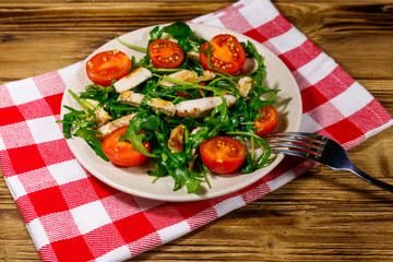 Tasty salad of fried chicken breast, fresh arugula and cherry tomatoes on wooden table