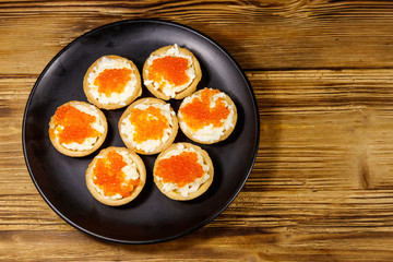 Tartlets with red caviar and soft cheese on a wooden table. Top view