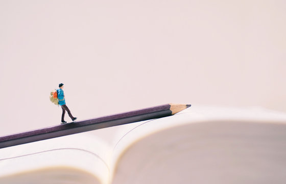 Miniature people figures with backpack walking on pencil and book with copy space, travel and study abroad concept