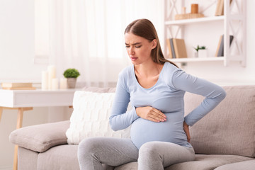 Expectant Woman Having Pain In Lower Back Sitting On Sofa