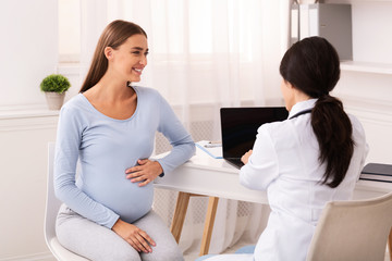 Smiling Pregnant Woman Talking With Doctor Sitting In Modern Office