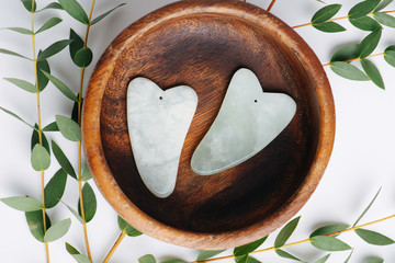 Fototapeta Top view of gua sha jade stones in wooden bowl over branches on white. obraz