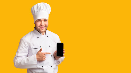 Positive Chef Holding Phone With Blank Screen Over Yellow Background