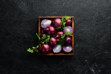 Purple onion in wooden box on black background. Top view. Free copy space.
