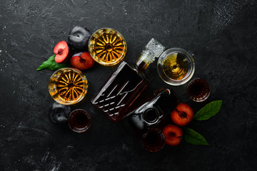 Slivovica - plum vodka, plum brandy in a bottle on a black stone table. Glasses with alcoholic beverage. Top view. Free space for your text.