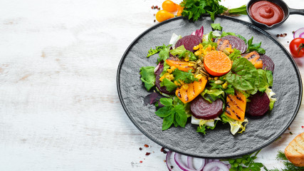 Salad: beetroot, pumpkin, corn and lettuce in a black plate on a white wooden background. Top view. Free space for your text.
