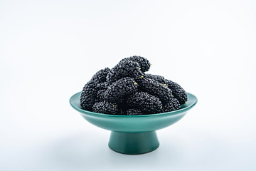 Dark green tall plate filled with fresh mulberries on white background