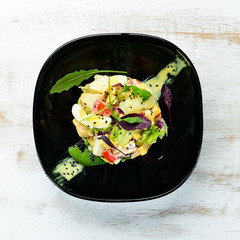 Vegetable salad with chicken, egg and mayonnaise sauce on a black plate. Top view. Free space for your text.