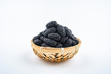 A bamboo dish filled with fresh black mulberries on a white background