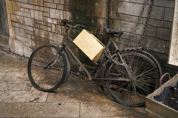 Fototapeta na wymiar Unused rusty old black bicycle with wooden box parked near dirty brick wall