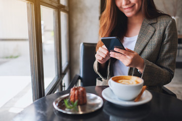 Closeup image of a woman holding and using mobile phone with coffee cup and snack on the table in cafe