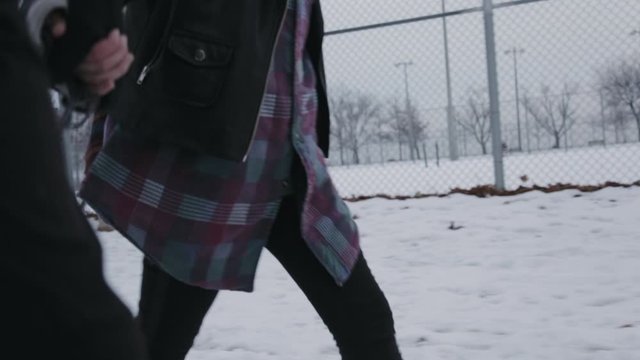 A Parent And A Child Walking Briskly Along The Snowy Terrain Holding Hands Together - Close Up Shot