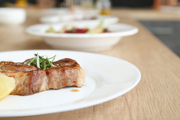 Plate with tasty cooked steak on table in kitchen