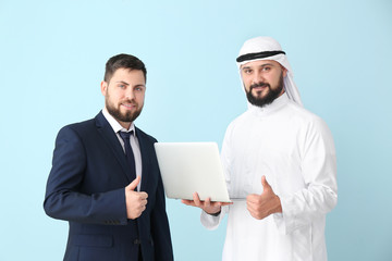 Arab man and his business partner with laptop on color background