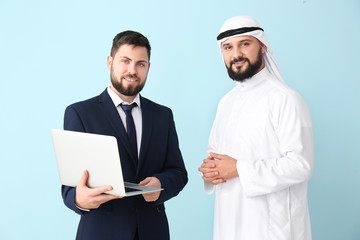 Arab man and his business partner with laptop on color background
