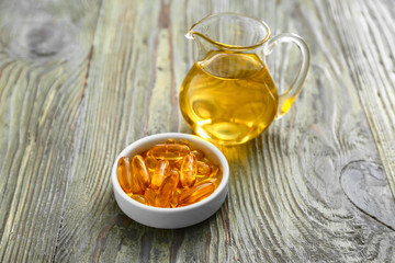 Jug of fish oil and capsules on wooden background