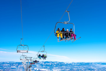 Skiers on ski lift at mountain ski resort with beautiful sky and mountains in the background