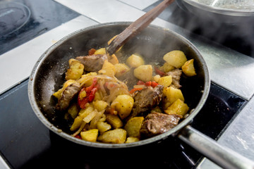 Chef cooks fried potatoes with pieces of meat in a restaurant kitchen