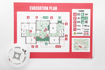 Evacuation plan and smoke detector on white background