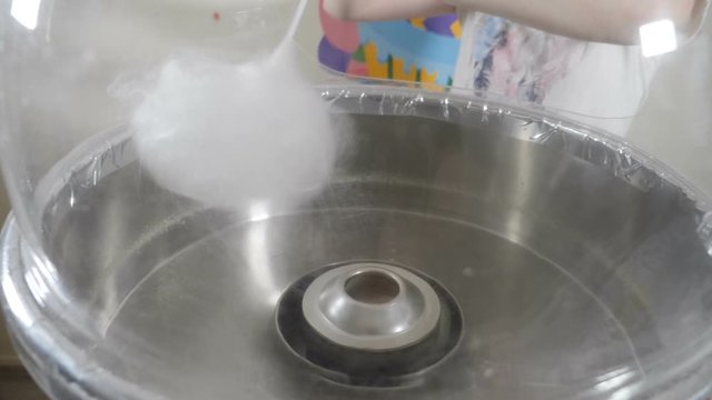 Female hand rolling cotton candy in candy floss machine. Making sweet candyfloss. Candy floss machine with white fairy floss . People make cotton candy for children during holiday. Slow motion. Full