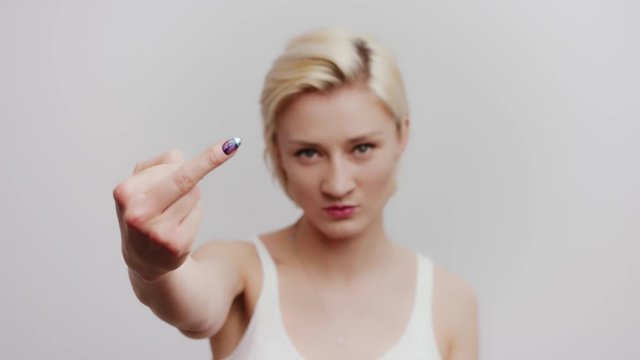 Hand gesticulation. Blonde angry young woman showing the middle finger. Studio shot isolated on white background, head and shoulders portrait