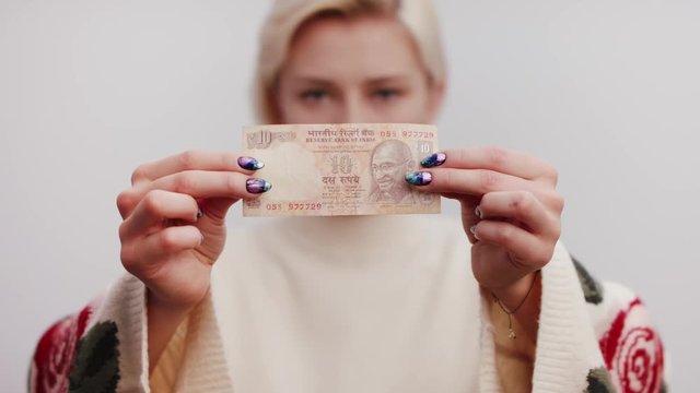 Indian Currency Rupee in the hands of the beautiful blonde woman. Close up shot of the banknote selective soft focus on, white background studio shot