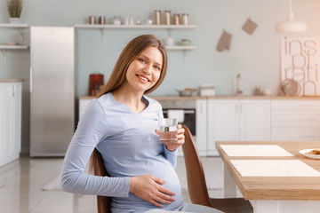 Fototapeta na wymiar Beautiful pregnant woman with glass of water in kitchen