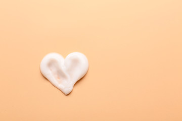 Heart made of cream on color background