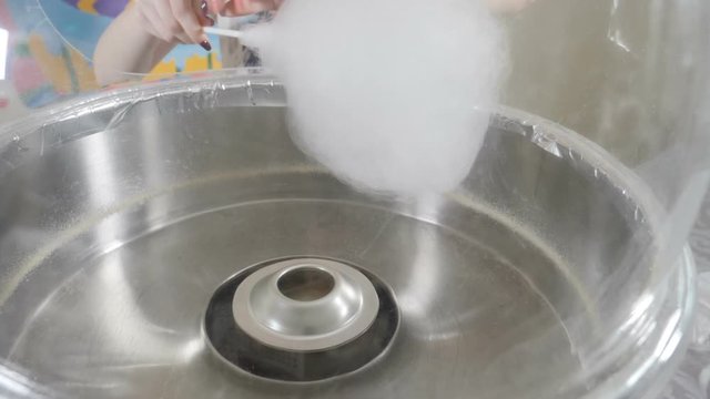 Close-up of an unrecognizable woman making candyfloss at children fair in slow motion. Working cotton candy machine. Full hd