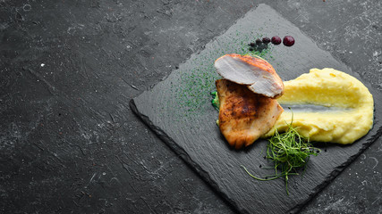 Baked chicken fillet with mashed potatoes on a black stone plate. Top view, free space for your text. Rustic style.