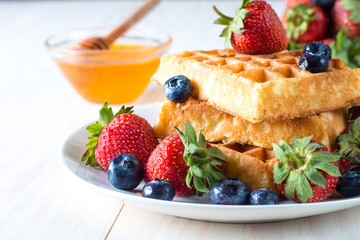 Fresh homemade food of berry Belgian waffles with honey, chocolate, strawberry, blueberry, maple syrup and cream. Healthy dessert breakfast concept with juice