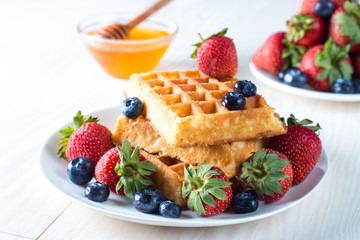 Fresh homemade food of berry Belgian waffles with honey, chocolate, strawberry, blueberry, maple syrup and cream. Healthy dessert breakfast concept with juice