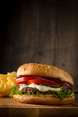 Home made hamburger with beef, onion, tomato, lettuce and cheese. Fresh burger close up on wooden rustic table with potato fries, beer and chips. Cheeseburger.