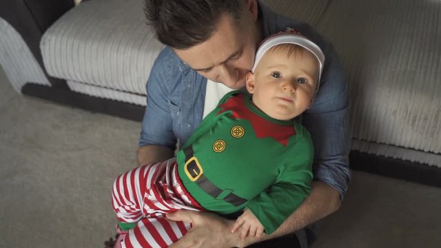 Dad playing with young son in elf costume while sitting on floor. Baby sitting on lap of daddy sharing snuggle and play time together. Fatherhood, parenting concept. Bonding with child.