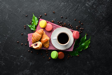 Breakfast. Coffee, croissant and macaroons. On a black stone background. Top view. Free space for your text.